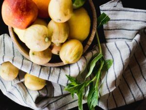 A wooden bowl filled with various citrus fruits sits on a striped cloth, evoking the vibrant freshness of casual fine dining, with a few lemons and fresh mint leaves artfully placed beside the bowl.