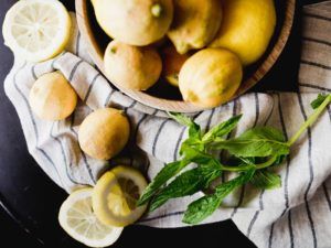 A bowl of lemons sits on a striped cloth with fresh mint leaves and lemon slices scattered around, evoking the bright and rustic charm of casual fine dining.