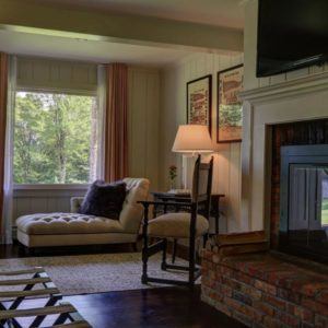 A cozy living room with a chaise lounge by a window, a small desk and chair beside it, a table lamp, framed art featuring the phrase carpe diem, a brick fireplace, and a TV mounted above the mantel.