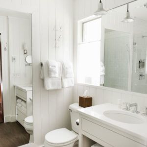 A bright, white bathroom with a large mirror, vanity, sink, toilet, and neatly folded towels invites you to simply let it be—a clean, minimalistic space filled with natural light.