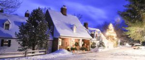 A cozy house covered in snow at night, with a lit Christmas tree outside, glowing windows, and a parked car. The peaceful scene mirrors the charm of winter and the magical things to do in Stowe VT beneath a blue-hued sky.
