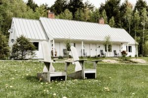 Two wooden chairs sit on a grassy lawn in front of a white house with a metal roof—an inviting scene typical of Vermont luxury hotel accommodations, surrounded by trees and lush greenery.