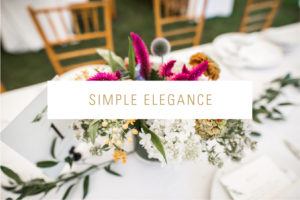 A floral centerpiece with white, pink, and purple flowers sits on a white table—perfect for weddings—with wooden chairs in the background. The words Simple Elegance are overlaid in gold text.