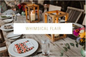 A rustic wooden table is set for weddings with plates, glasses, candles in wooden lanterns, and colorful napkins. Flowers add a lively touch. The words “Whimsical Flair” appear across the center.