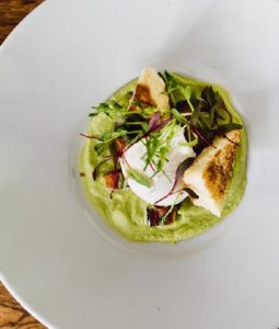 A white plate with green pea puree, topped with a poached egg, toasted bread slices, and microgreens, artfully arranged in the center—a perfect example of casual fine dining presentation.