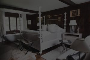 A cozy Edson Hill bedroom with dark wood walls, a four-poster bed with white bedding, a bench at the foot, a nightstand with a lamp, and a freestanding bathtub near a window with white curtains.