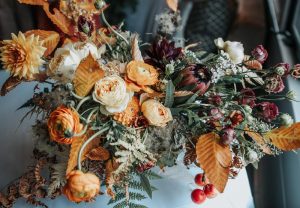 A vibrant autumn bouquet featuring orange, yellow, and white flowers, accented with dried leaves, ferns, and red berries—reminiscent of the warm charm found at Edson Hill - Stowe Vermont Inn—arranged on a light surface with a soft, blurred background.