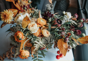 A vibrant autumn bouquet with yellow, orange, and burgundy flowers, mixed with ferns, dried leaves, and red berries, arranged on a light surface near a window—evoking the cozy charm of Edson Hill - Stowe Vermont Inn.