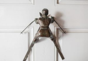 A metal door handle shaped like a person in a crouched position, with arms and legs spread, adds charm to a white wooden door—an artistic detail reminiscent of the unique touches at Edson Hill - Stowe Vermont Inn.