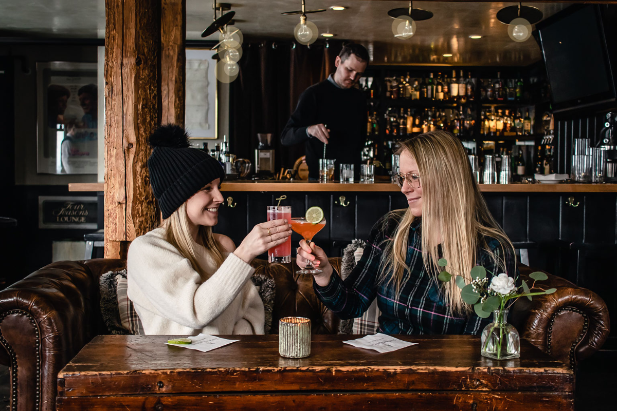 Women enjoying cocktails, bartender prepares drinks at bar