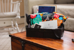 A black gift basket with popcorn snacks, a greeting card labeled Edson Hill - Stowe Vermont Inn, and a postcard sits on a wooden table in a cozy living room.