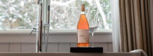 A bottle of rosé wine and an empty wine glass sit on a tray by a window with snowy trees outside. White curtains frame the scene, creating a cozy atmosphere perfect for relaxing after exploring our new Reservation Enhancements.