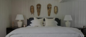 A neatly made bed with white bedding is centered between two dark nightstands, each with a white lamp. Above the bed, three snowshoes decorate the white-paneled wall, evoking cozy Stowe VT Resort charm.