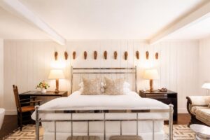 Bright Edson Hill bedroom with a metal-frame bed, white bedding, two dark nightstands with lamps, decorative pillows, wall art above the bed, a desk with a chair, and a sofa on the right.