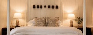 Cozy bedroom in a Vermont luxury hotel, featuring a white comforter, two patterned pillows, and two bedside tables with matching lamps. Decorative items adorn the wall above the bed, while soft, warm lighting fills the space and creates an inviting atmosphere.
