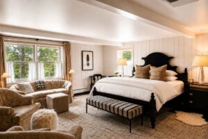 Bright, cozy bedroom with a large bed, two armchairs, a small sofa, a striped bench, lamps, and large windows letting in natural light. Light walls and carpet create a warm, inviting atmosphere—perfect for relaxing after exploring with one of our exclusive vacation packages.