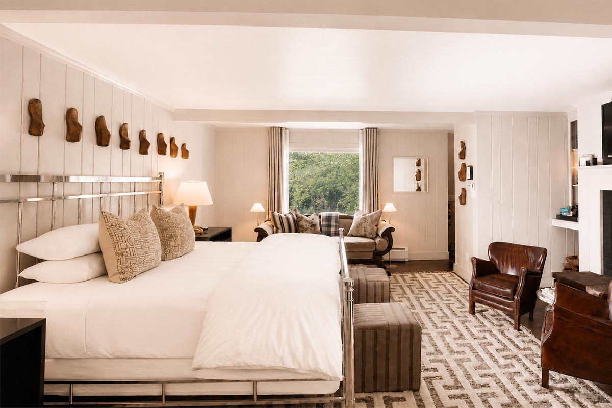 Bright, elegant hotel room with a large bed, armchairs, ottomans, a patterned rug, wall art, and a window with garden views—creating a cozy and welcoming atmosphere—perfect for guests enjoying exclusive vacation packages. Bright, elegant hotel room with a large bed, armchairs, ottomans, a patterned rug, wall art, and a window with garden views—creating a cozy and welcoming atmosphere—perfect for guests enjoying exclusive vacation packages.