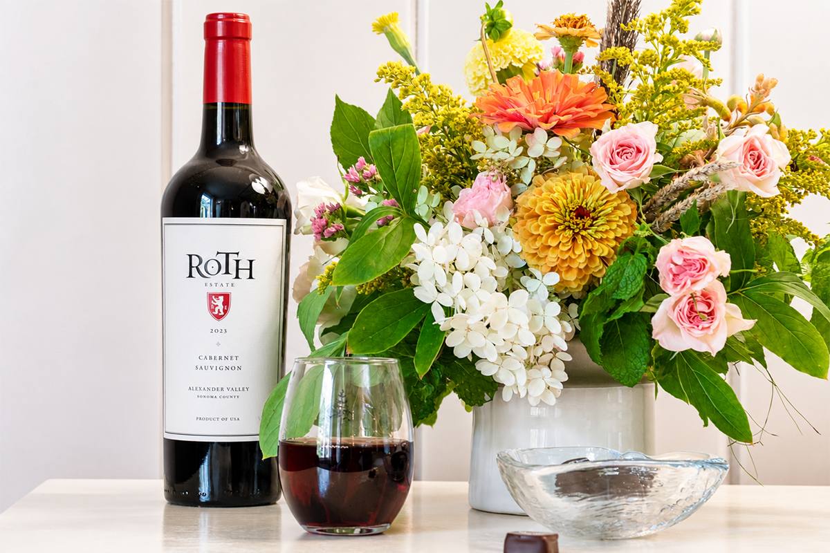 A bottle of Roth Cabernet Sauvignon wine, a glass of red wine, a bowl, and a colorful bouquet of flowers on a white table against a light background evoke the relaxed elegance found in curated vacation packages. A bottle of Roth Cabernet Sauvignon wine, a glass of red wine, a bowl, and a colorful bouquet of flowers on a white table against a light background evoke the relaxed elegance found in curated vacation packages.