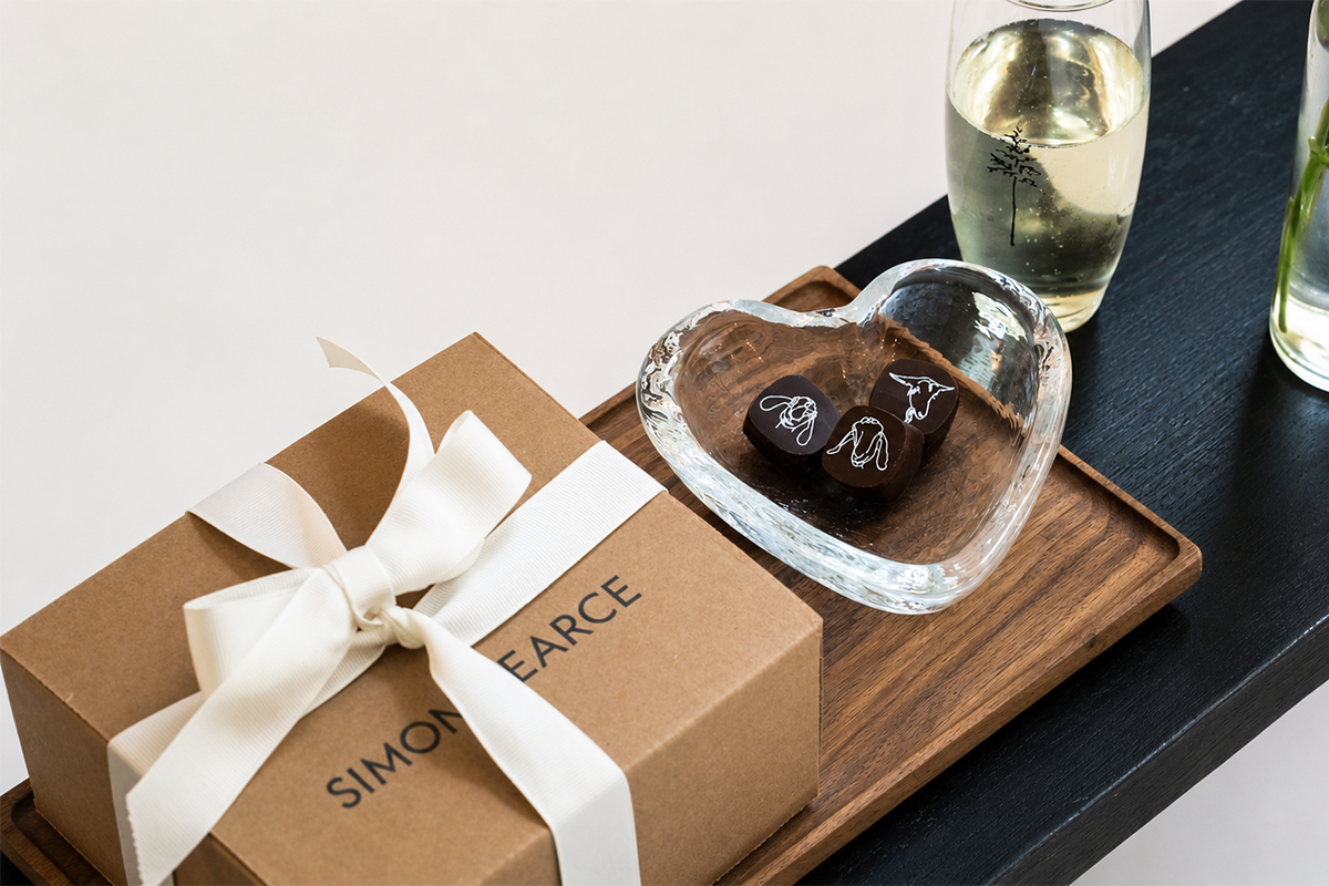 A brown gift box with a white ribbon, a heart-shaped glass dish holding two chocolates, and a glass of champagne on a wooden tray—perfect touches to inspire dreams of romantic vacation packages. A brown gift box with a white ribbon, a heart-shaped glass dish holding two chocolates, and a glass of champagne on a wooden tray—perfect touches to inspire dreams of romantic vacation packages.