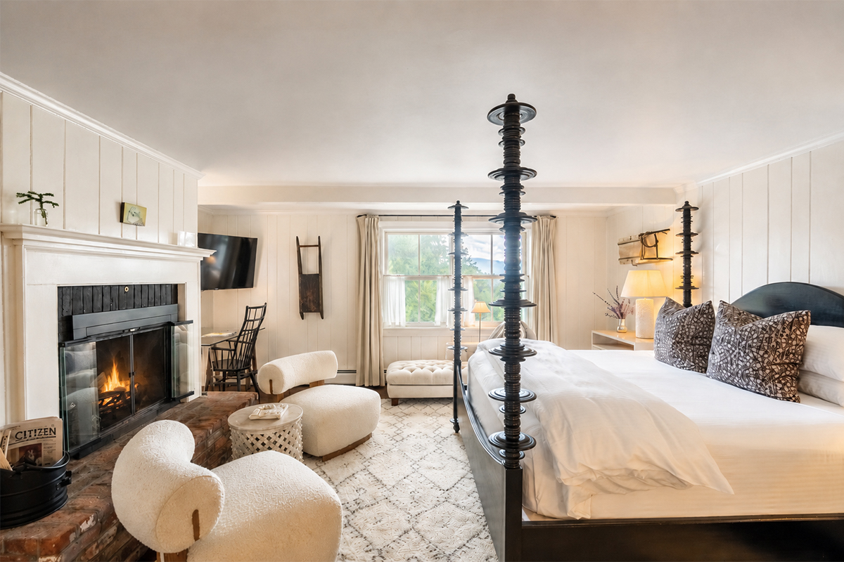 A cozy bedroom with a four-poster bed, fireplace, cream chairs, soft rug, window with curtains, and modern decor—all in neutral tones—creates a warm and inviting atmosphere perfect for relaxing after exploring one of our exclusive vacation packages. A cozy bedroom with a four-poster bed, fireplace, cream chairs, soft rug, window with curtains, and modern decor—all in neutral tones—creates a warm and inviting atmosphere perfect for relaxing after exploring one of our exclusive vacation packages.